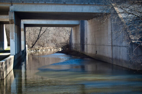 Paxton Creek flows calmly under a large overpass.