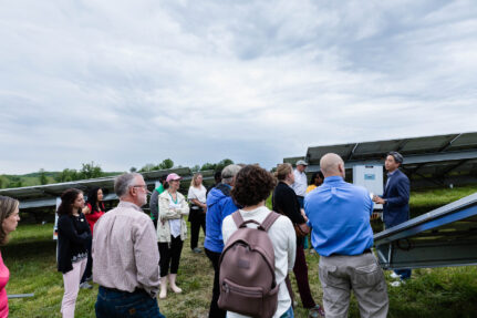 Group of people gather outside around solar panels.