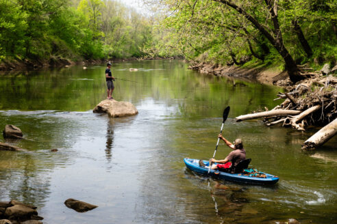 Dennis Radigan of Aberdeen, Maryland, paddles his kayak into Deer Creek at Susquehanna State Park in Harford County, Maryland, while a man fishes from a nearby rock.