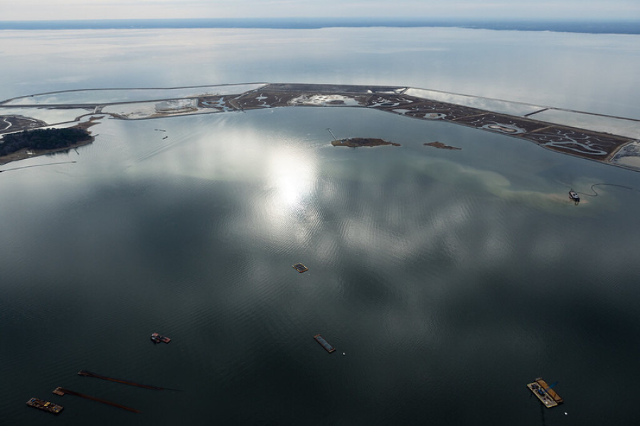 Sun shines off the Chesapeake Bay as seen from the air. A thin strip of land sits in the foreground.