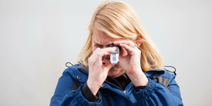 A woman holds a refractometer up to her eye.